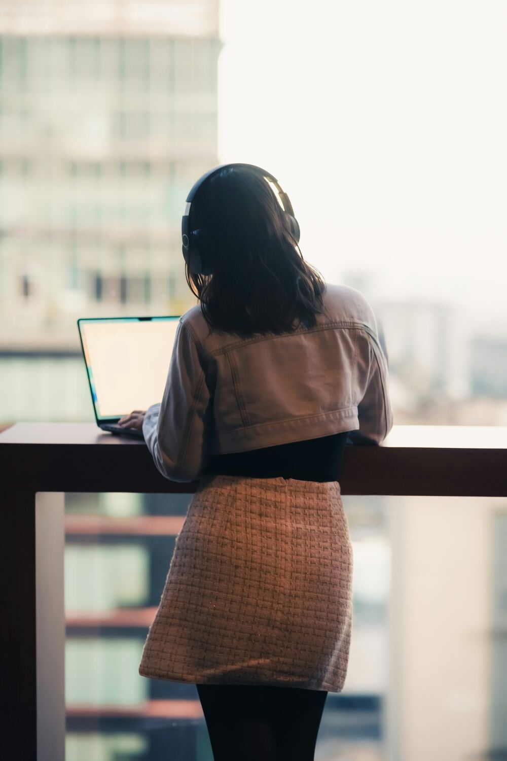 A woman wearing headphones joins a session on her laptop from a bright, quiet spot by the window
